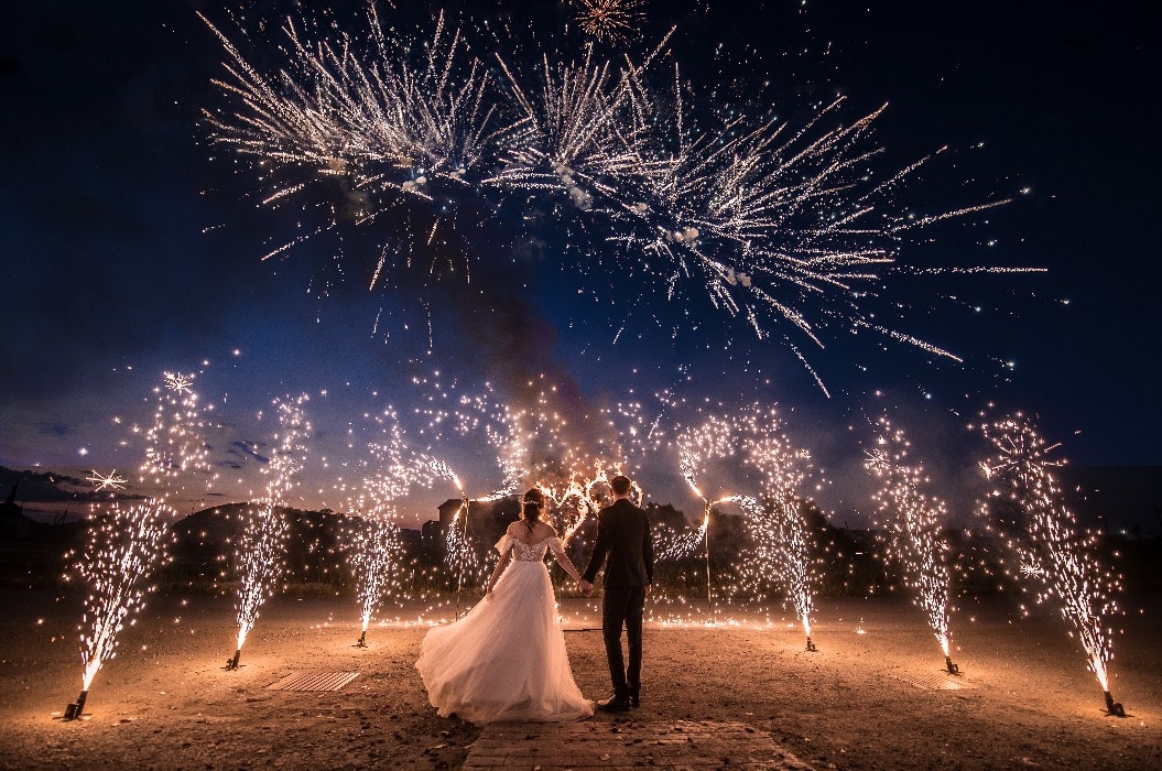 A couple in wedding dresses on the background of fireworks at night.